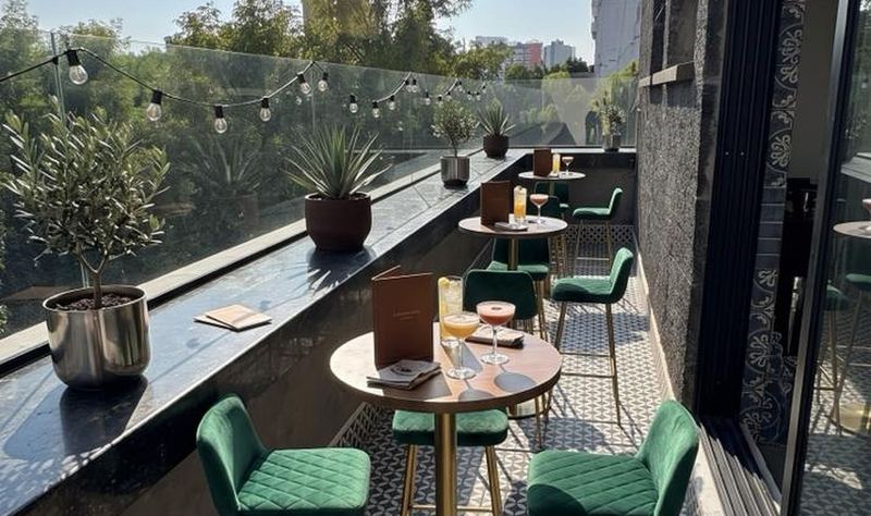 Terraza Puebla con mesas altas, sillas de terciopelo verde y vegetación